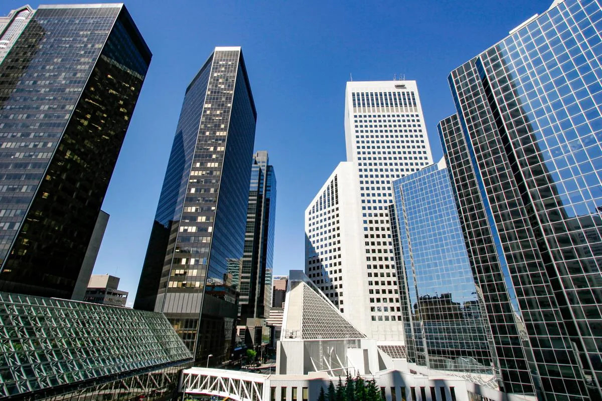 Cluster of modern high-rise office buildings under a clear blue sky. The image showcases a mix of sleek black and mirrored glass façades alongside distinct white geometric architecture, reflecting the city’s business district skyline.